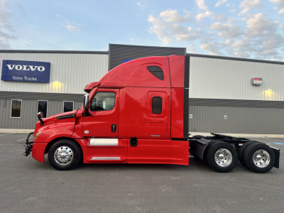 Red 2022 Freightliner Cascadia 126 semi-truck side view with sleeper cab, chrome wheels, in-service vehicle, stock sign in background.