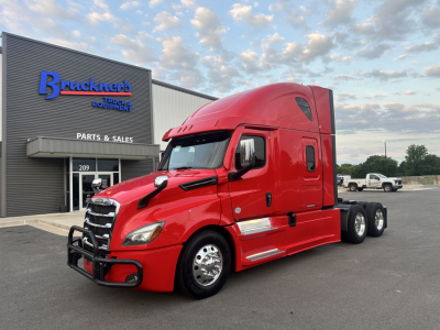 Freightliner Cascadia 126 tractor in red parked outside a service building with blue 'Bruckner's' sign; text on building reads PARTS & SALES and 209 door; no other labels clearly visible.