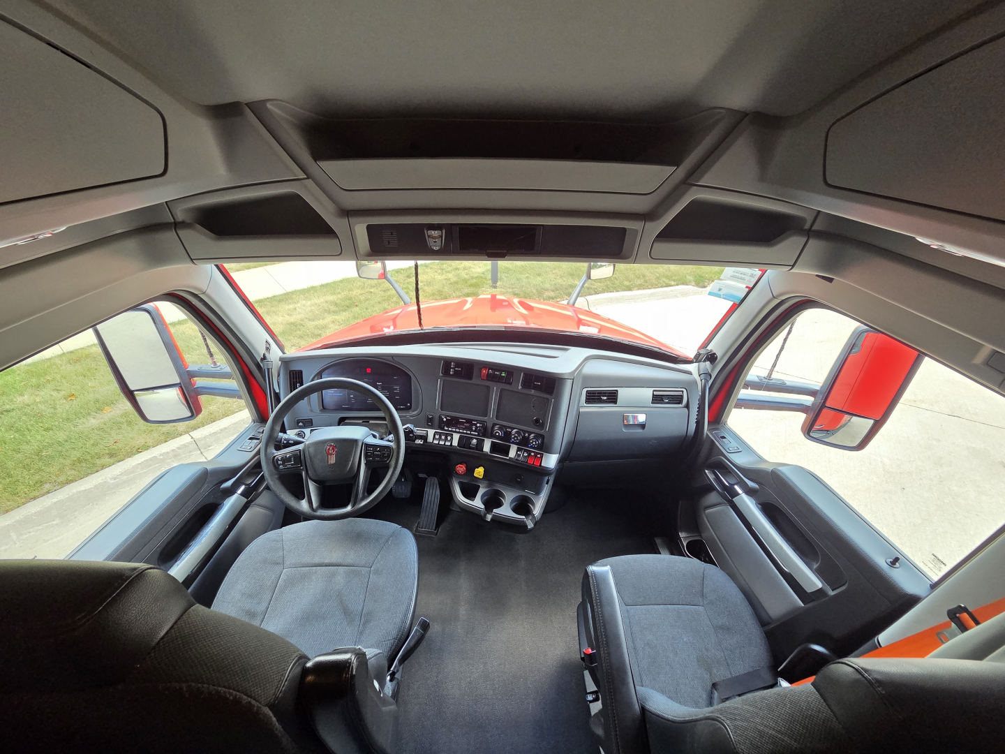 Interior of a 2024 Kenworth T680 cab showing driver seat, steering wheel, dashboard, center console, and passenger seat in view