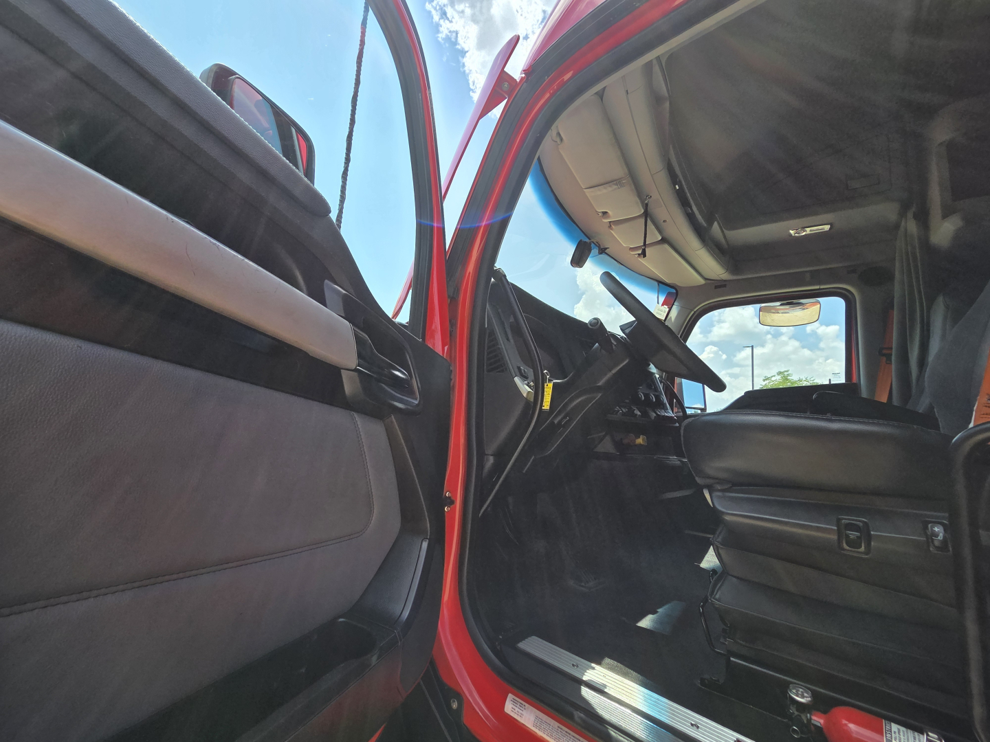 Kenworth T680 truck cabin interior view from open driver door showing steering wheel, dashboard, and seat in an in-service truck.