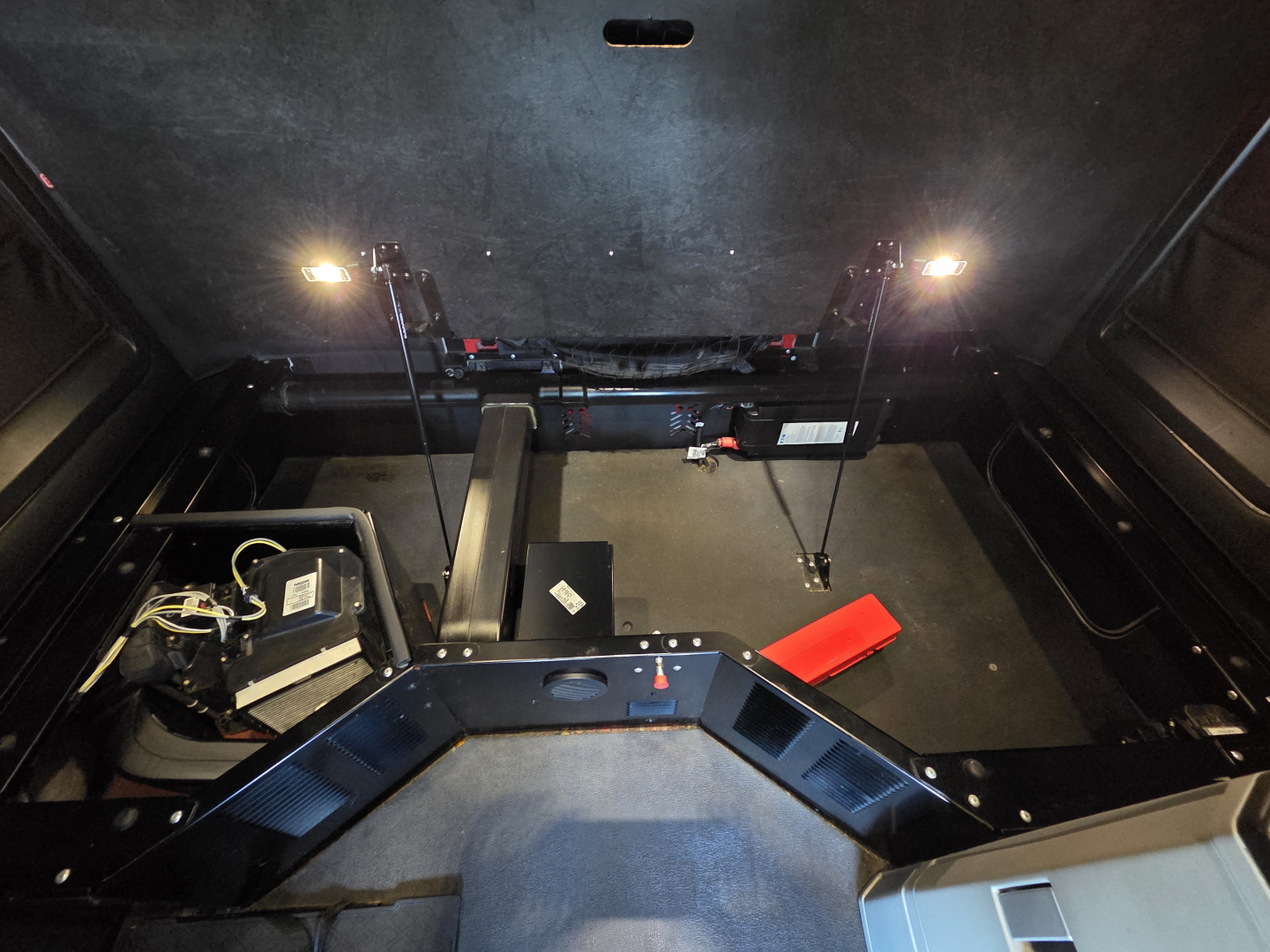 Kenworth T680 truck interior cargo area view with rear storage and toolkit, showing black components and wiring.