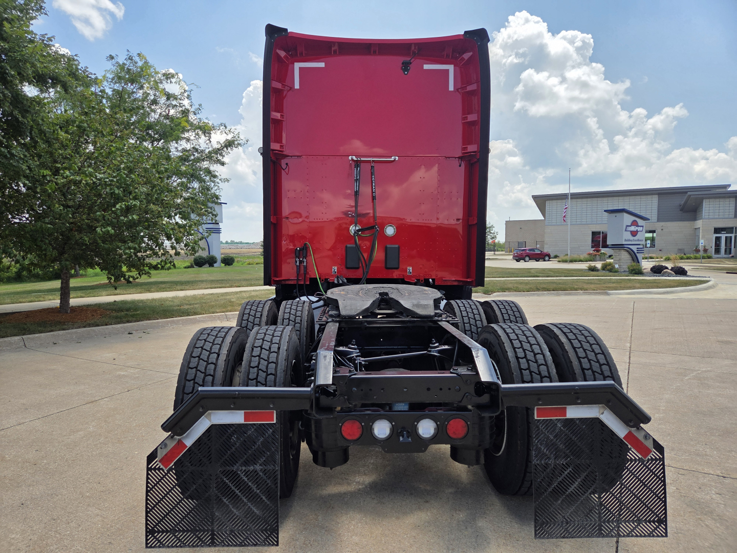 Kenworth T680 rear tractor view showing fifth wheel, dual rear axles, and mud flaps with stock photos. Red sleeper cab with rear door open.