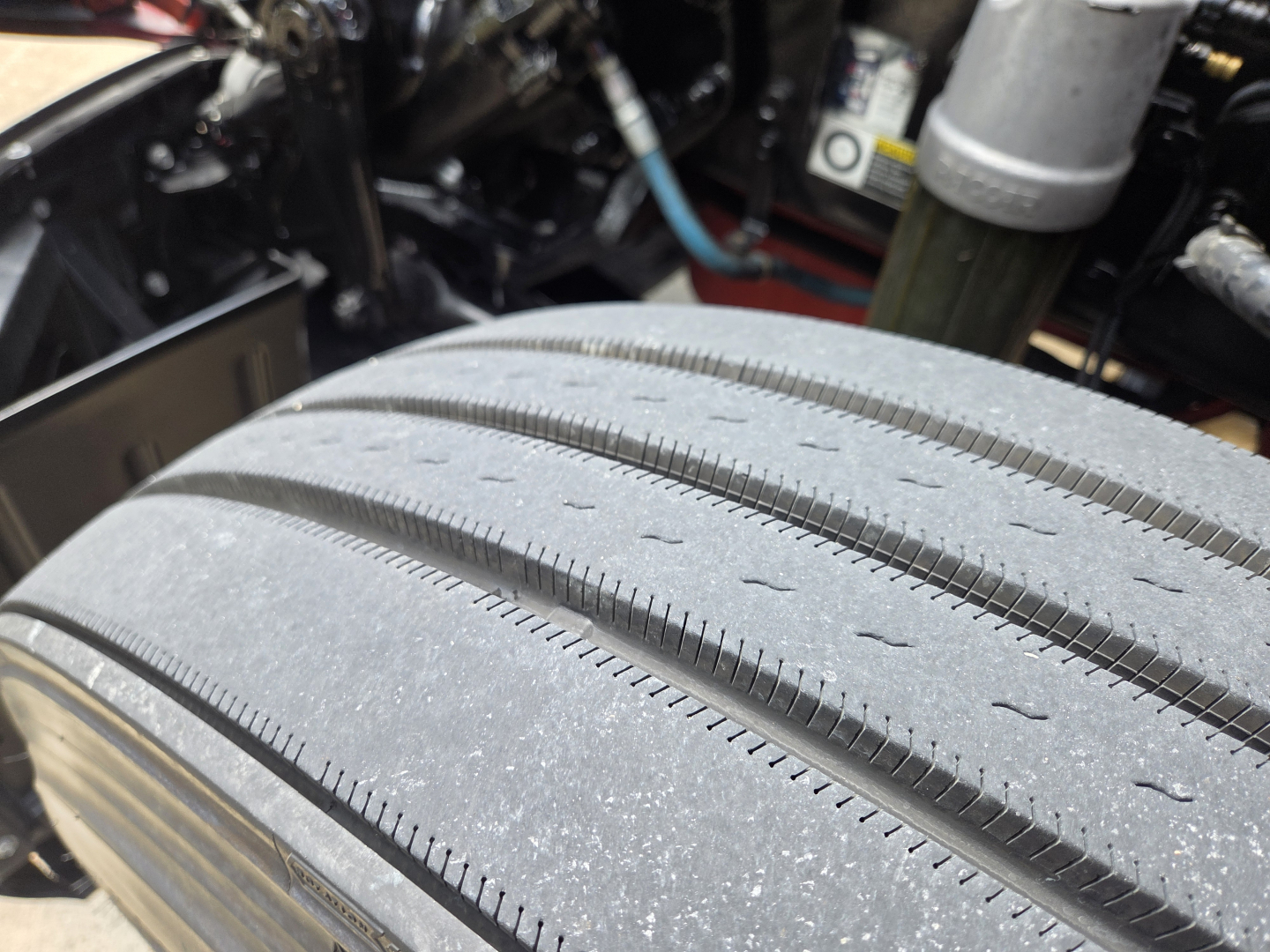 Tire tread close-up on Kenworth T680 engine bay area showing road-worn tire with visible grooves and dust.