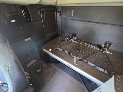 Kenworth T680 cab interior with a raised sleeper bed platform, side storage panels, and cargo straps visible.