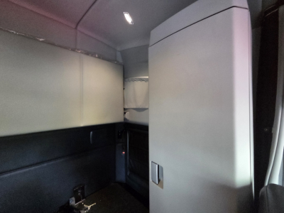 Kenworth T680 cab interior showing sleeper area with vertical storage cabinet and dim overhead light.