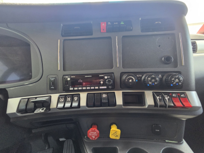 Kenworth truck dash with multiple control switches, climate controls, and dashboard display; engine start and auxiliary switches visible.