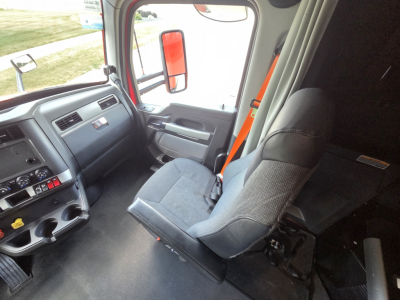Kenworth T680 interior cab view showing driver seat, steering area, dashboard, and orange driver seat belt in a sleeper truck.