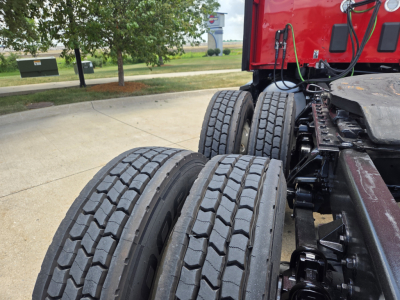 Kenworth T680 truck chassis rear view showing dual rear axles and tires, red cab visible in background.