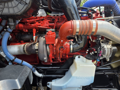 Kenworth T680 engine bay showing red diesel turbocharged engine and air intake with blue coolant reservoir hoses.
