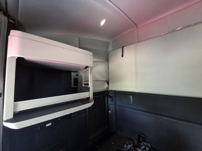 Kenworth T680 sleeper cab interior with bunk bed and overhead storage shelf, showing cabin paneling and dim lighting.