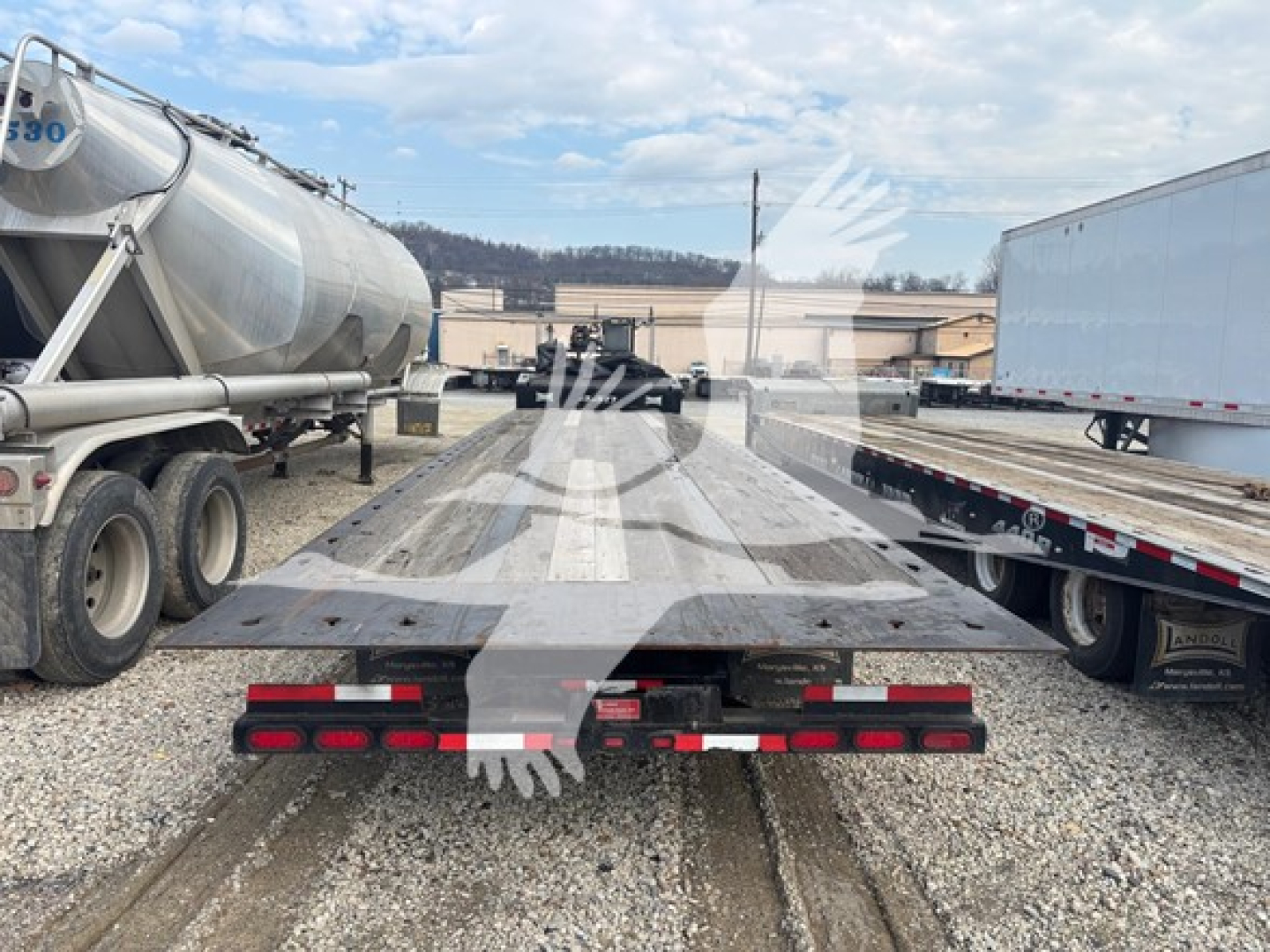 Flatbed trailer deck with Landoll logo silhouette watermark, viewed from rear showing wooden deck, fenders, and dual-axle wheels; industrial yard in background.