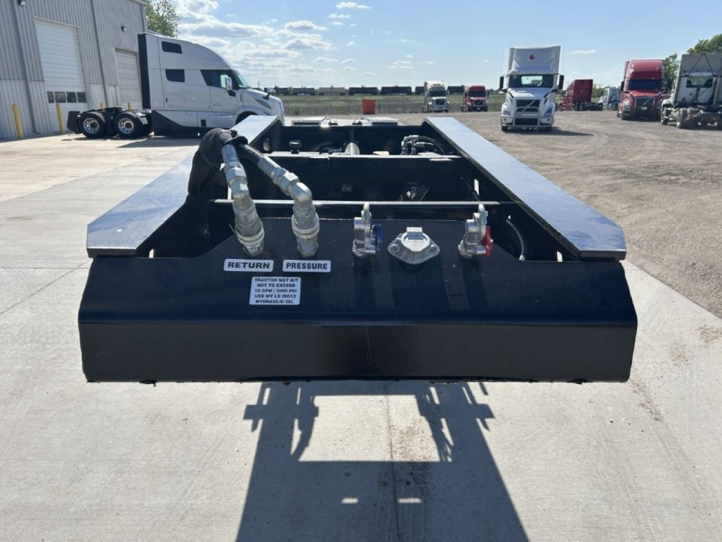 Lowboy trailer hitch area showing hoses, fittings, and couplings with labels: RETURN and PRESSURE, on black metal frame.