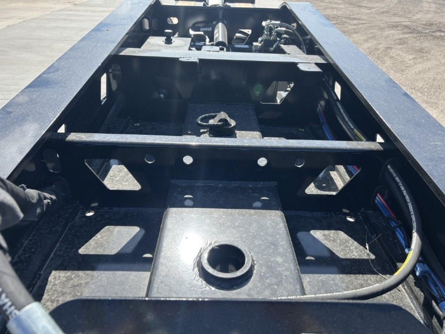 Trailer frame showing undercarriage with structural beams and hose lines; circular opening and mounting points visible on a steel deck.
