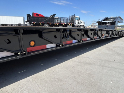 Trailer side view showing lowboy deck with black painted steel framing and reflective red/white safety markings along the edge.