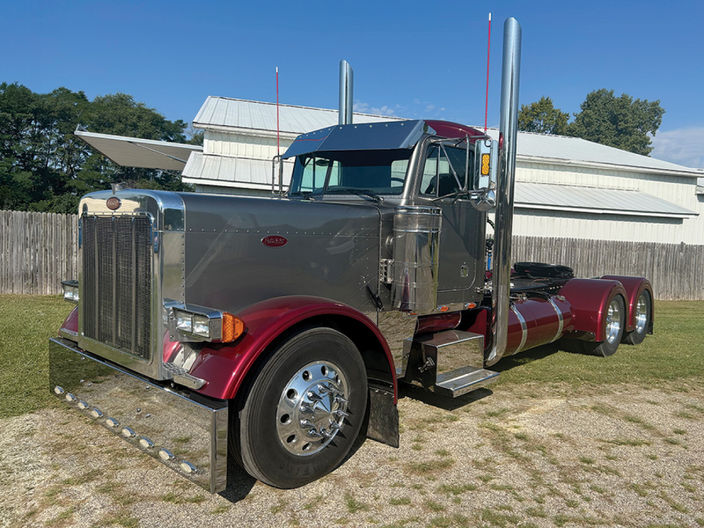 Peterbilt 379 conventional daycab truck in service with gray cab and maroon fenders, chrome grille, tall exhaust stacks, and dual rear axles visible.