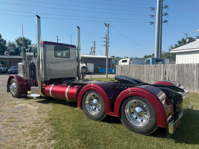 Peterbilt 379 conventional daycab tractor showing chrome exhaust stacks and maroon fenders with dual rear axles and polished wheels.