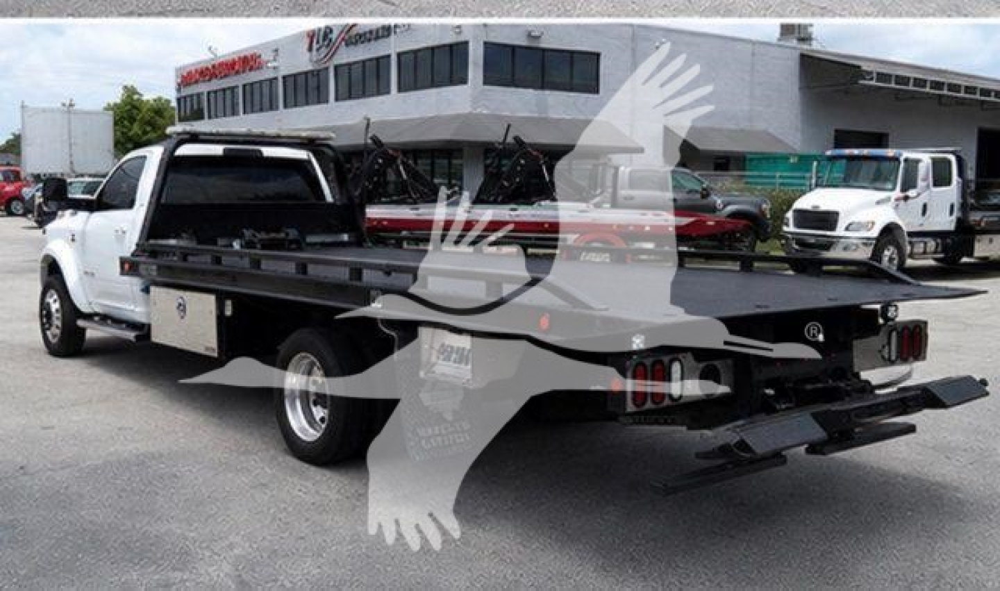 Back of a white 2021 Ram 5500 rollback tow truck with a flatbed and rear ramps, dealership lot in background.