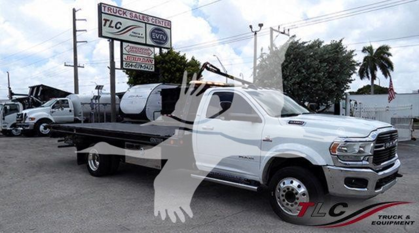 Ram 5500 rollback tow truck in a dealership lot with a flatbed and chrome dual rear wheels, windshield sticker, and TLC overlay mark.