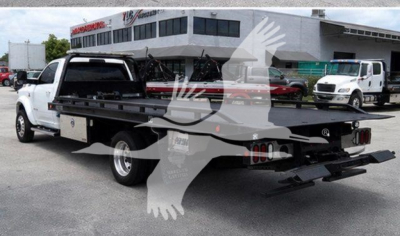 Back of a white 2021 Ram 5500 rollback tow truck with a flatbed and rear ramps, dealership lot in background.