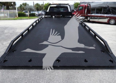 Flatbed tow truck bed with metal texture and a large white gull logo overlayed on the surface.