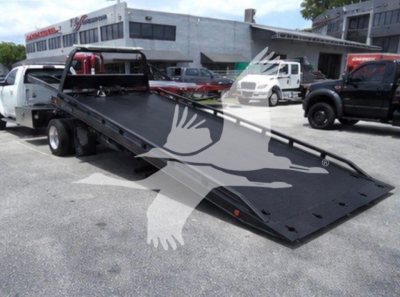 Ram 5500 rollback truck bed tilted at an angle with black surface and hydraulic ramp in a dealership lot.