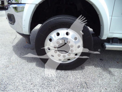 Wheel and front fender of a white Ram 5500 chassis cab showing a chrome multi-hole hubcap and tire, partial bumper and step rail visible.