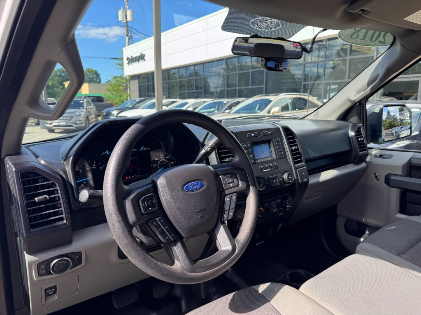 Ford F-150 interior view showing steering wheel with Ford logo, dashboard, center console, gear shifter, and front seats.