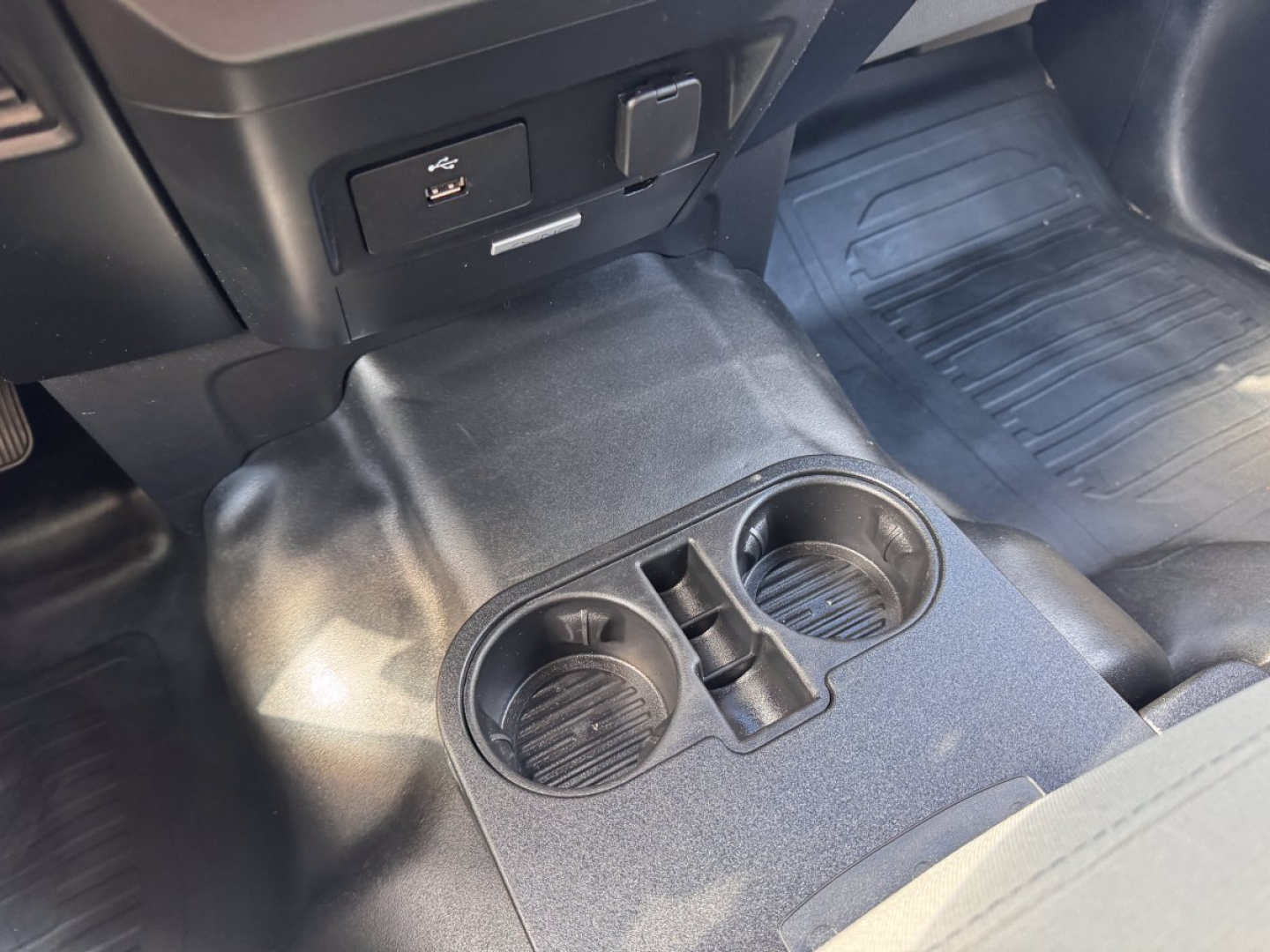 Ford F-150 cabin center console with two cup holders and a small storage slot, view of floor mats and lower dash area.