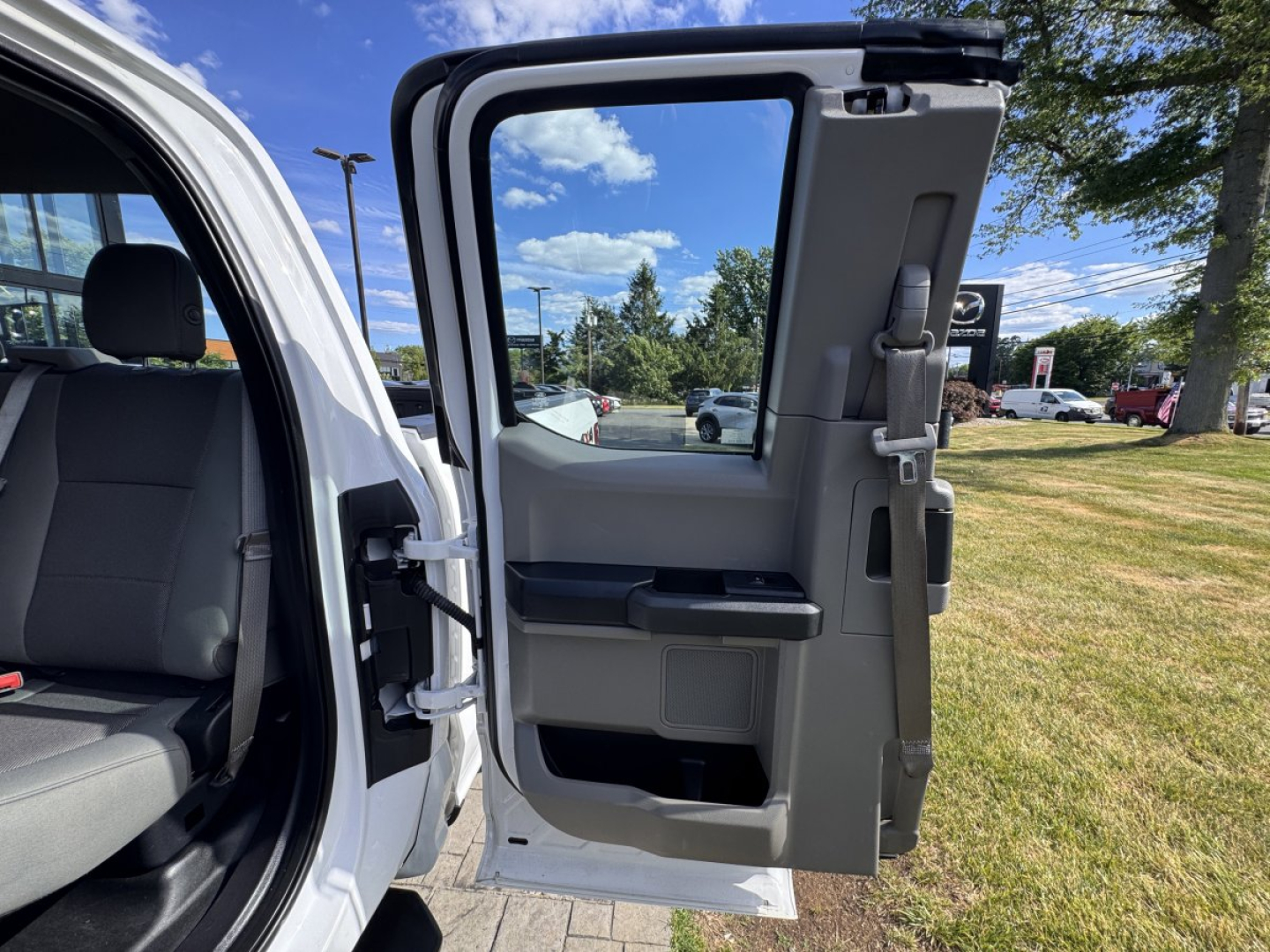 Truck door interior and open rear passenger door of a 2018 Ford F-150 showing grey interior panels and seatbacks, with the outside environment in a dealership lot.