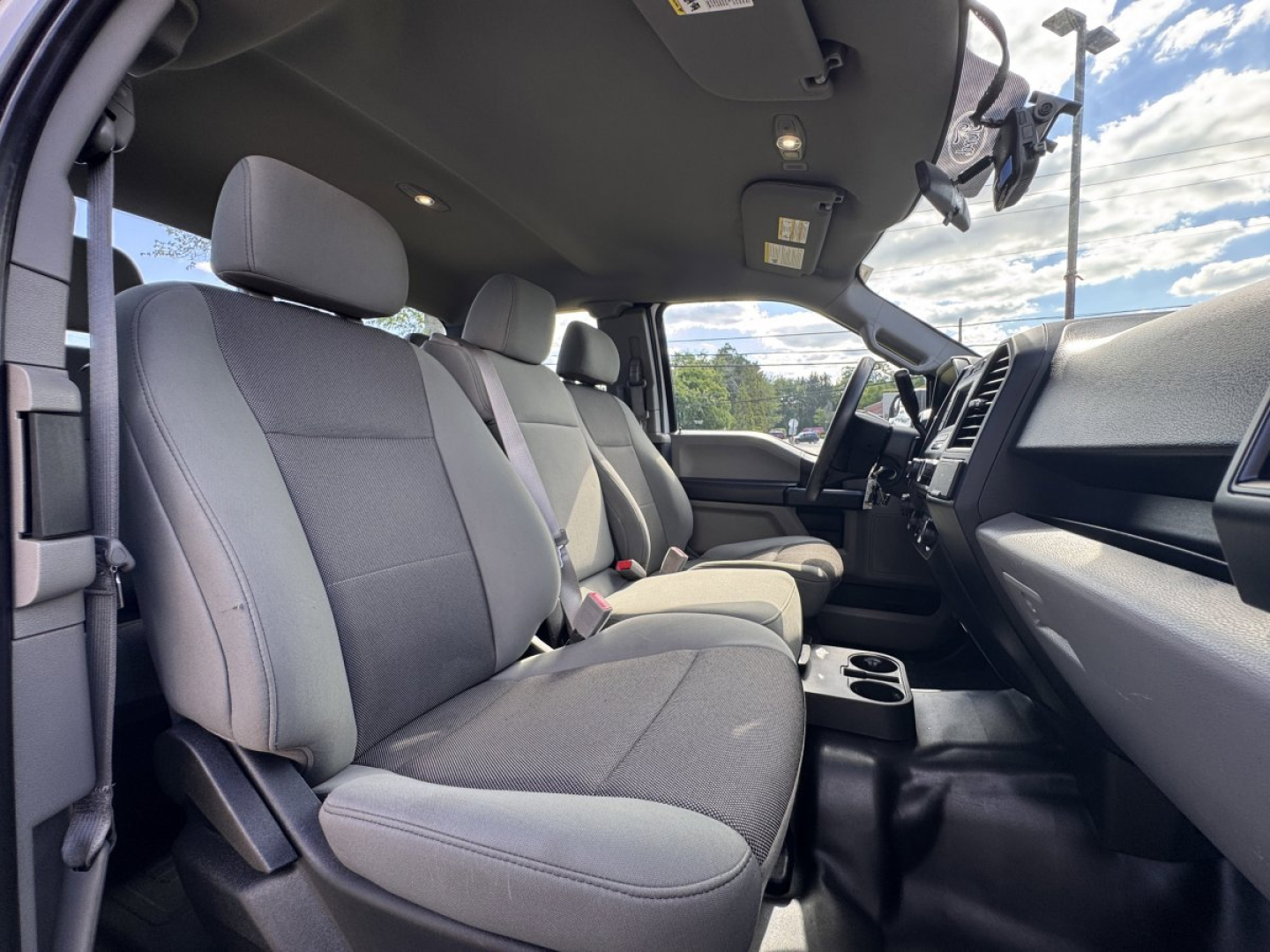 Ford F-150 interior front seats and dashboard view, with light gray cloth seats, center console, steering wheel, and front row doors visible.