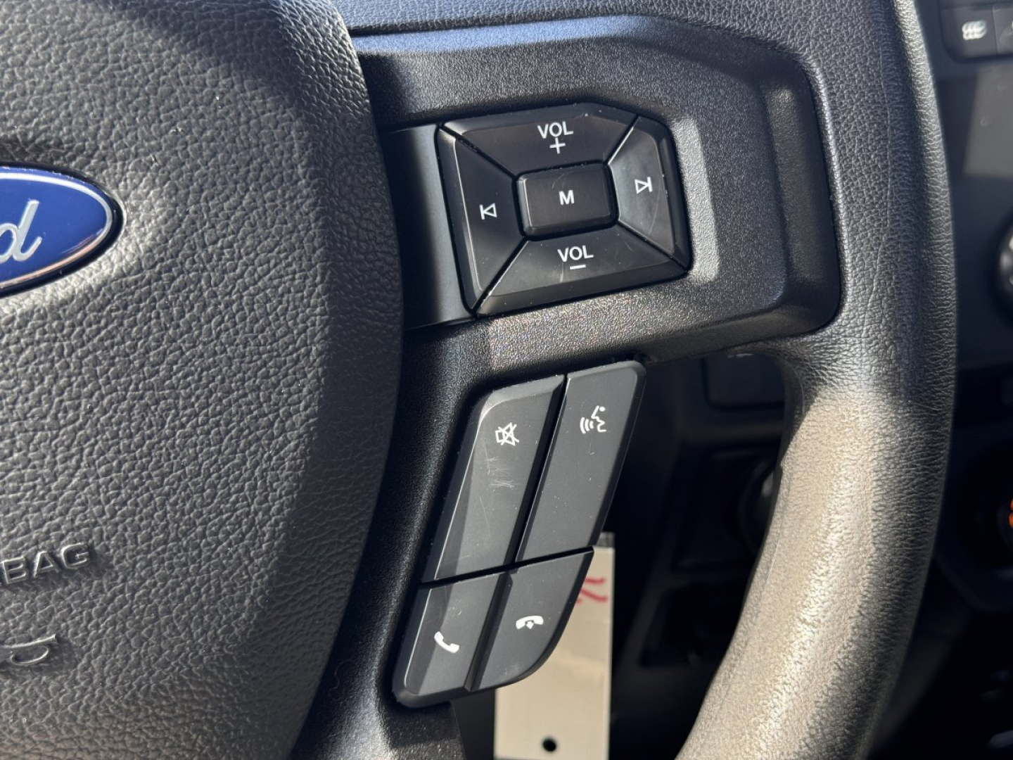 Ford F-150 steering wheel close-up with audio controls and phone buttons visible on the left spokes.