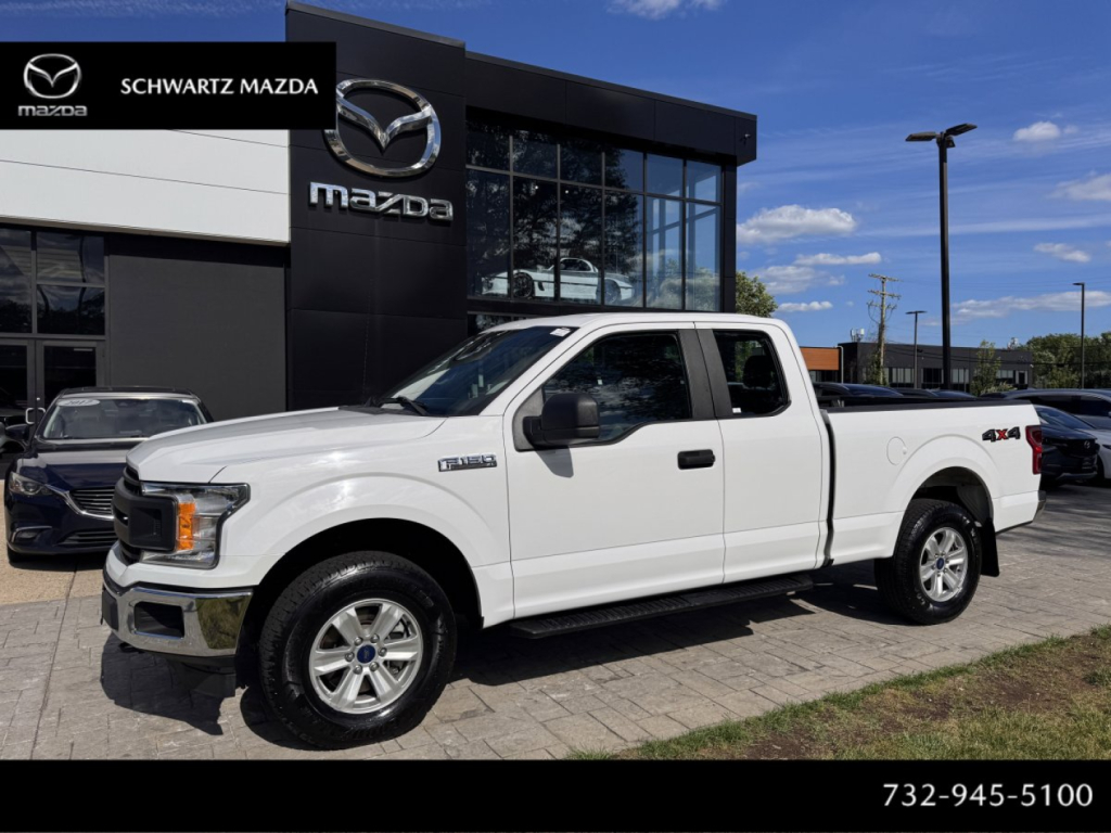 Ford F-150 pickup truck in white, extended cab, parked in dealership lot with Mazda branding in background; side view showing 4x4 badge on rear