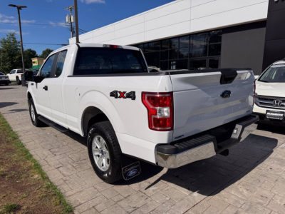 White 2018 Ford F-150 4x4 pickup truck rear three-quarter view showing 4x4 badge on rear fender and bed with dealership building in background.