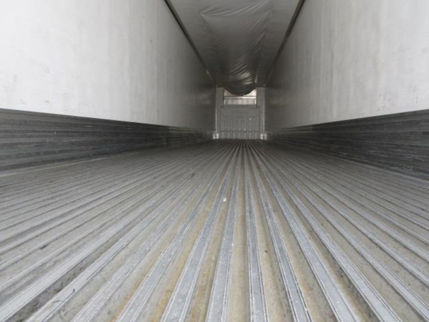 Inside of a refrigerated trailer cargo hold with ribbed floor and white walls, long tunnel perspective toward rear.