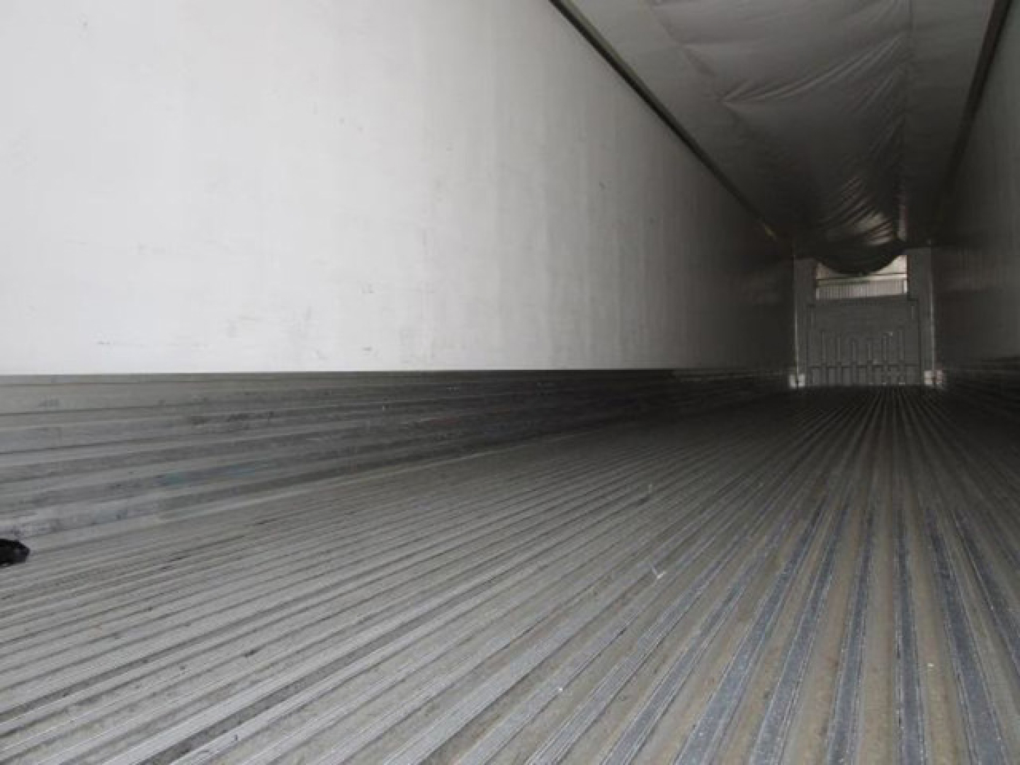 Trailer interior showing corrugated aluminum floor with ribbed texture, sidewall, and rear cargo door opening, for a refrigerated trailer.