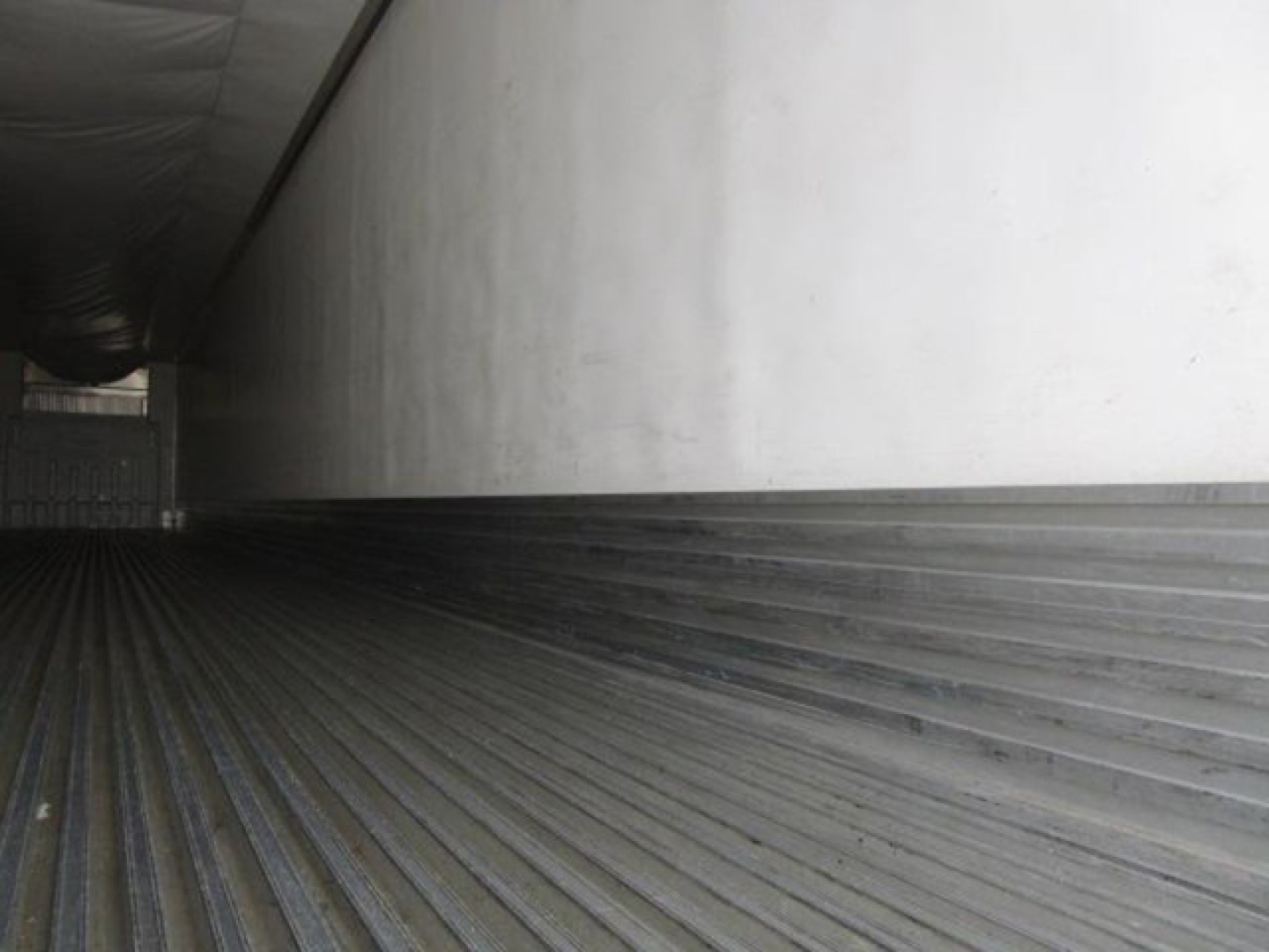 Trailer interior showing corrugated metal floor and a white side wall with black lower rail