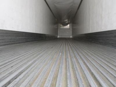 Inside of a refrigerated trailer cargo hold with ribbed floor and white walls, long tunnel perspective toward rear.