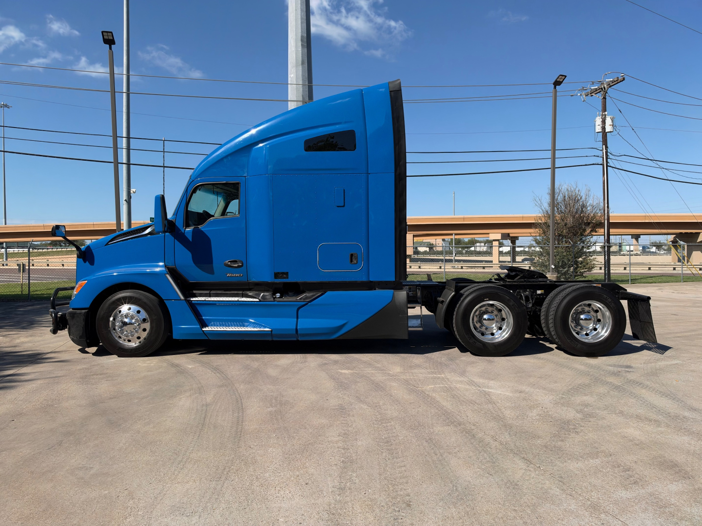 Blue Kenworth T680 tractor-trailer side view showing sleeper cab, two-axle rear, chrome wheels, and side mirrors.