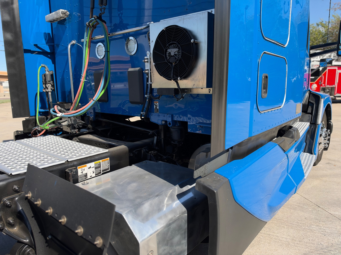 Kenworth T680 truck cab area showing cooling fan and metal toolbox with hoses and wiring harness in blue sleeper configuration