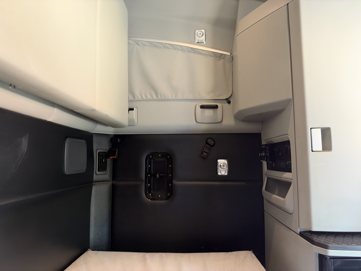 Truck cab interior showing sleeper area and dashboard components with a hatch and panels.