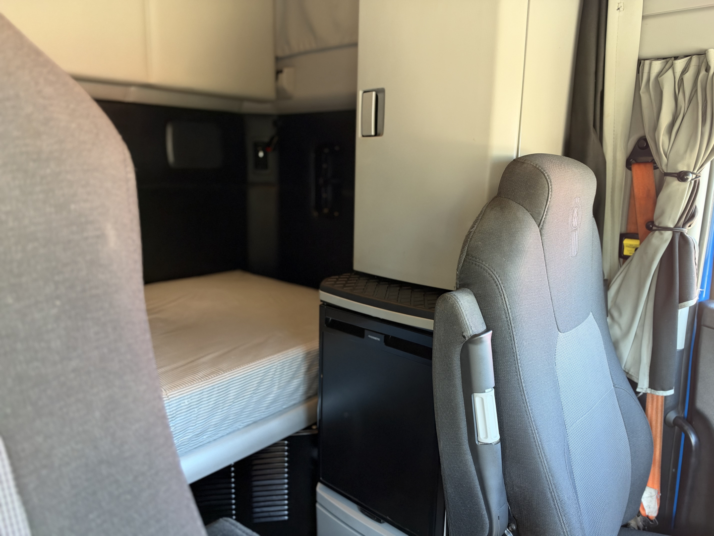 Kenworth T680 truck interior showing driver's seat and sleeper area with storage cabinet visible.