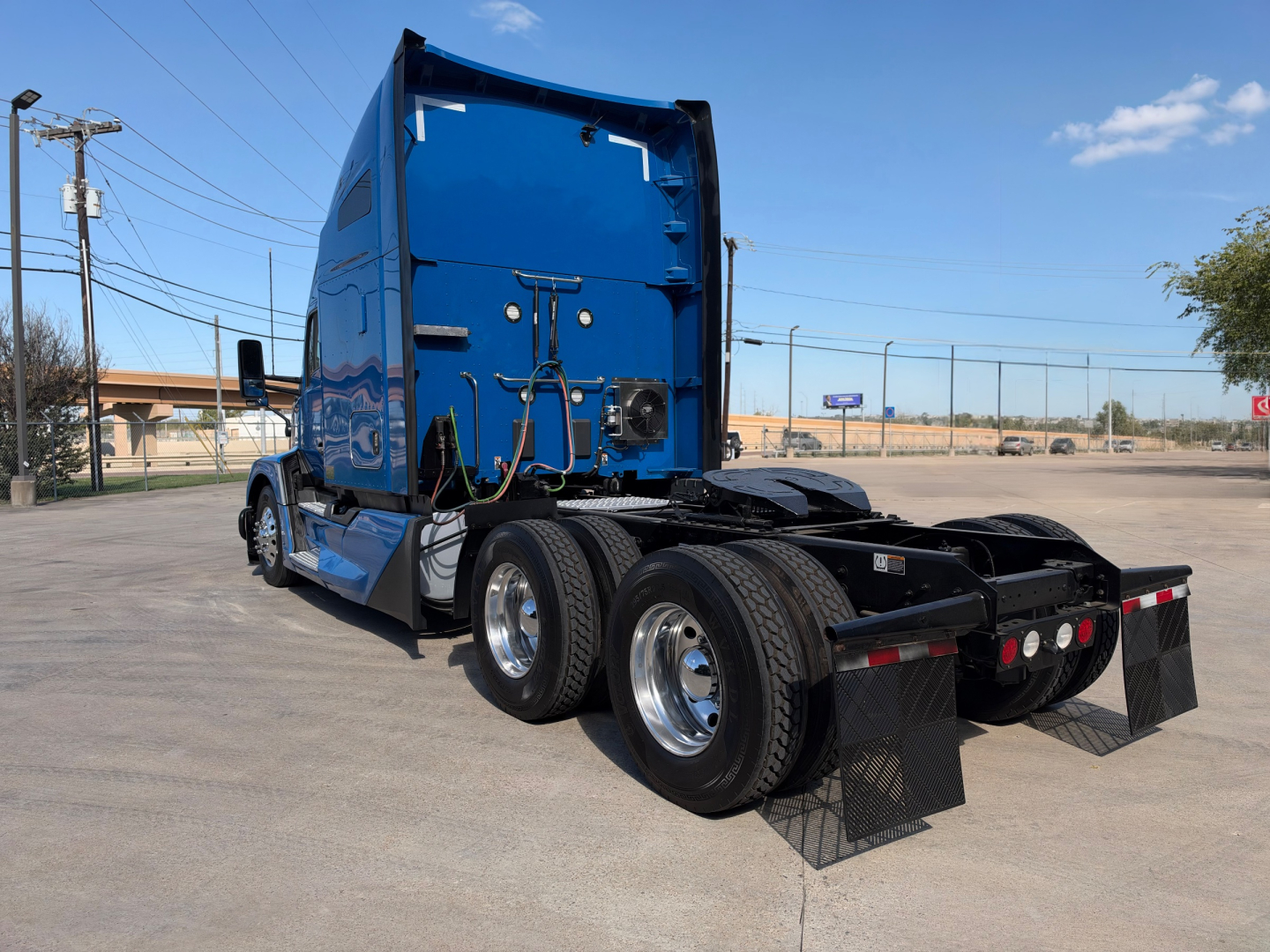 Kenworth T680 tractor rear angle showing dual rear axles, blue cab, and mud flaps.