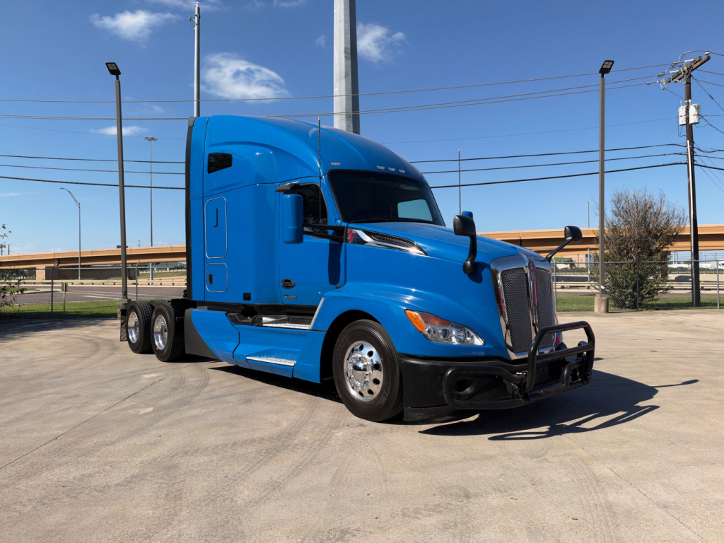 Truck cab: blue 2023 Kenworth T680 conventional sleeper showing front grille and side view mirrors.