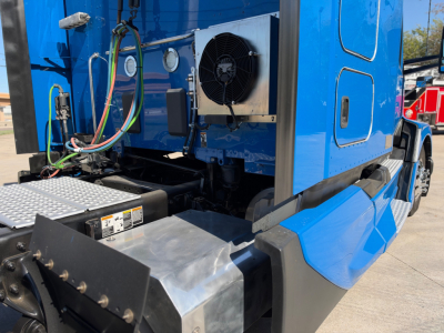 Kenworth T680 truck cab area showing cooling fan and metal toolbox with hoses and wiring harness in blue sleeper configuration