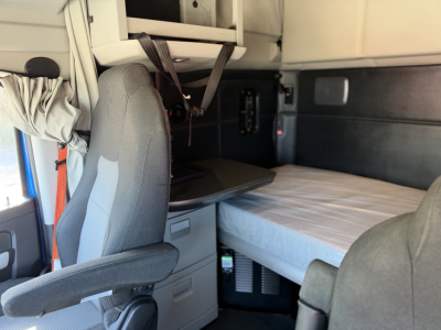 Kenworth truck cab interior showing sleeper bunk area with overhead storage and pilot chair.