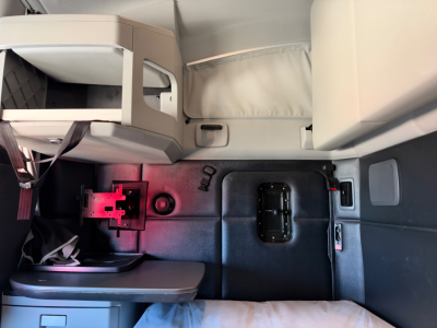 Interior sleeper area of a 2023 Kenworth T680 cab with storage compartments and a mounted monitor arm; visible panels and a doorway opening on the side.