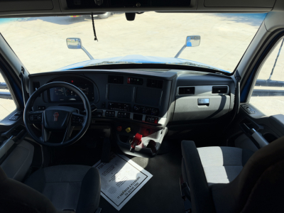 Kenworth T680 truck interior dashboard view with steering wheel and driver seat, windshield, side mirrors, and center console visible.