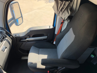 Interior of a Kenworth T680 cabin showing driver seat and dashboard with window and door panel visible.