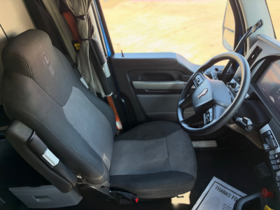 Kenworth T680 interior view showing driver seat, steering wheel, and dashboard from the cab with fabric seat and controls visible.