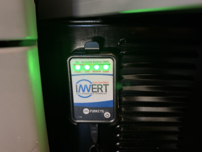 Device labeled Invert battery guard with green LEDs mounted on a Kenworth T680 engine bay near a black ribbed component.